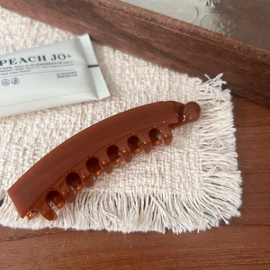 Detail of glossy brown pumpkin-shaped banana hair clip on a soft white tassel mat