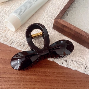 Close-up of elegant dark brown bow hair claw clip with a glossy finish and gold spring