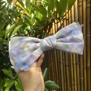 Floral chiffon bow hair clip with 3D blue butterflies against a garden background