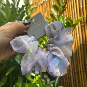 Close-up of a floral print organza scrunchie in light purple and blue held by a hand outdoors