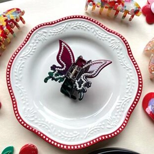 Close-up of a dark green hair claw with gradient purple butterfly wings and pearls