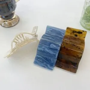 Three acetate hair claws including beige hollow, blue wave, and tortoise patterns