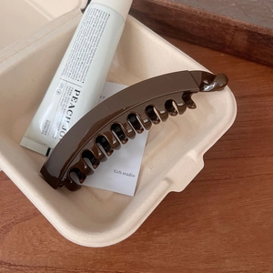 Close-up of a glossy brown resin claw clip on a minimalist wooden background display