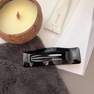 Close-up of a glossy black rectangular hollow hair claw clip on a cozy table setting