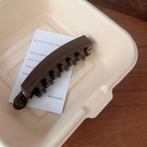 Close-up of deep brown banana hair clip with sleek interlocking teeth on a cream tray