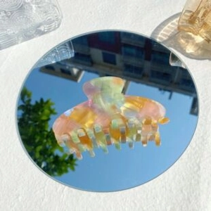 Macro detail of a colorful marble acetate hair claw clip reflected on a mirror surface