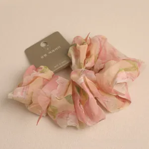 Detailed view of a pink floral scrunchie made of translucent chiffon on a paper card