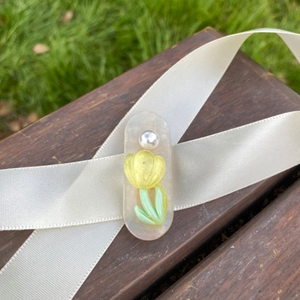 Detail of tulip floral duckbill hair clip with pearl on elegant cream ribbon background