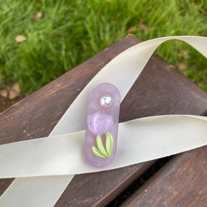 Detail view of purple tulip hair clip with pearl decoration on dark wood and white ribbon
