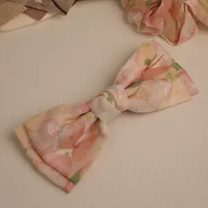 Detailed view of floral chiffon bow hair clip with butterfly pattern on cream surface