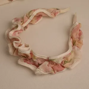 Close-up of a pink floral ruffled headband with white trim and delicate layered pleats
