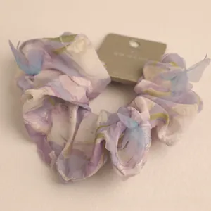 Close-up of floral fabric hair scrunchie with light blue butterfly accessory on white card