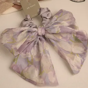 Detailed view of a purple floral tulip pattern organza bow scrunchie with a product tag