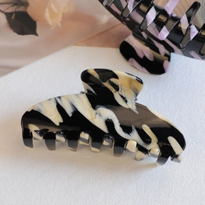 Detailed view of large marbled acetate hair claw clip with glossy black and cream wavy pattern