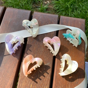 Outdoor shot of six colorful heart-shaped acetate hair claws on a wooden bench
