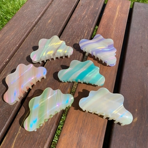 Set of six colorful cloud-shaped acetate hair claws on a wooden bench in natural sunlight