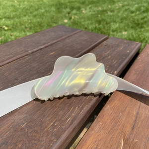 Detailed view of cloud-shaped iridescent acetate hair claw clip on wooden bench outdoors