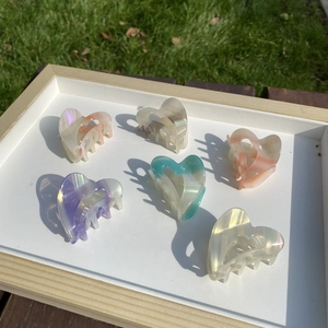 Detailed view of six colorful heart-shaped acetate hair claws on a white tray outdoors