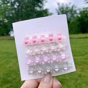 Detail of four candy-colored bear hair clips with pink hearts on a white card display