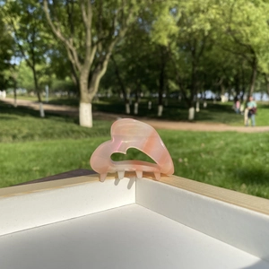 Detail of peach heart-shaped acetate hair claw clip with marble texture on wooden tray
