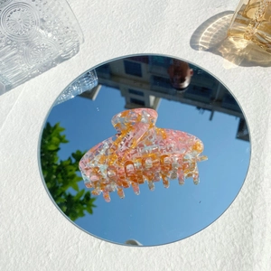 Haarklammer aus Acetat mit buntem Blumenmuster auf einem runden Spiegelboden