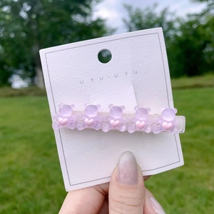 Cute purple bear hair clip with pink hearts on a card with outdoor grass background