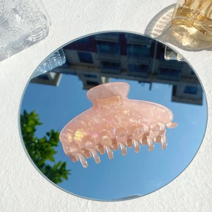 Macro detail of peach pink iridescent resin hair claw clip with glitter finish on a mirror