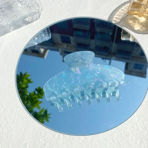 Macro detail of large translucent light blue claw clip with iridescent glitter on mirror