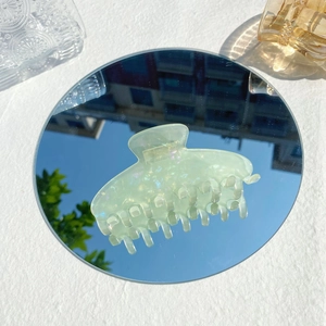 Detail of light green acetate hair claw with iridescent shimmer on a mirror surface