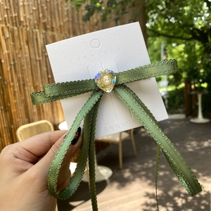 Detail of green ribbon bow hair clip with heart cameo pendant on display card