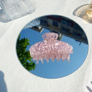 Haarklammer aus pinkem Acetat mit Marmormuster spiegelt sich auf einem runden Spiegel