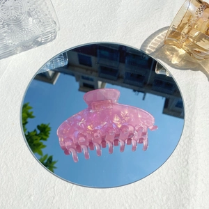 Macro detail of a pink translucent claw clip with pearlescent glitter on a mirror surface