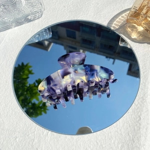 Iridescent purple acetate hair claw clip reflected on mirror with sky background