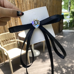 Close-up of a black lace bow hair clip with a cameo heart pendant on a white card