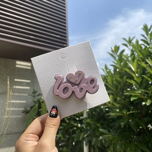 Detail of pink LOVE hair clip with embedded rhinestones on white display card