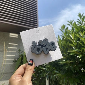 Close-up of a grey acetate LOVE hair clip with heart detail and sparkling rhinestones