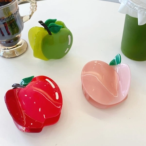 Détail des pinces à cheveux pomme rouge et pêche rose en acétate sur un plan blanc