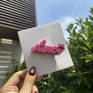 Close-up of pink Amor letter hair clip with rhinestone detail on display card