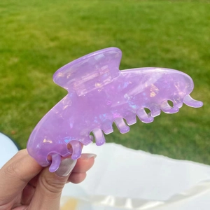 Close-up of a large purple iridescent hair claw clip with glitter finish held outdoors