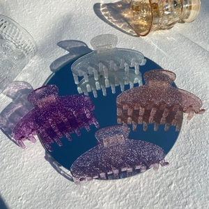 Macro detail of large acetate hair claws in iridescent purple shades on a mirror tray