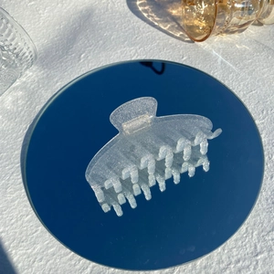 Macro detail of a translucent frosted hair claw clip with fine silver glitter on a mirror