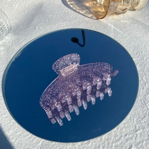 Detail of pink pearlescent hair claw clip with glitter finish on a reflective mirror