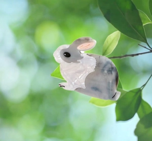 Détail d'une pince à cheveux lapin en acétate parmi des feuilles vertes au style naturel