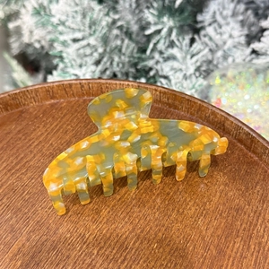 Macro shot of large amber-patterned acetate hair claw clip on a dark wooden base