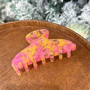 Detailed view of large marbled iridescent acetate hair claw on a decorative wooden tray