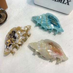 Close-up of three seashell hair claws in blue, brown, and pearl white marble finish