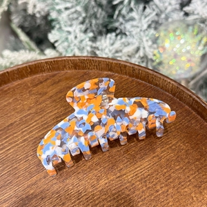 Macro shot of large acetate claw clip with colorful floral pattern on a wooden plate