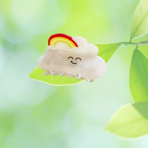 Detail of cute white cloud hair claw with rainbow pattern and smile on green leaf