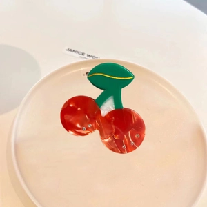 Cute cherry shaped acetic acid hair claw clip with rhinestones on a white ceramic plate