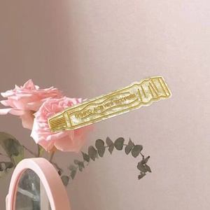 Creative toothpaste tube hair clip in pearly white acetate with gold details and floral motifs